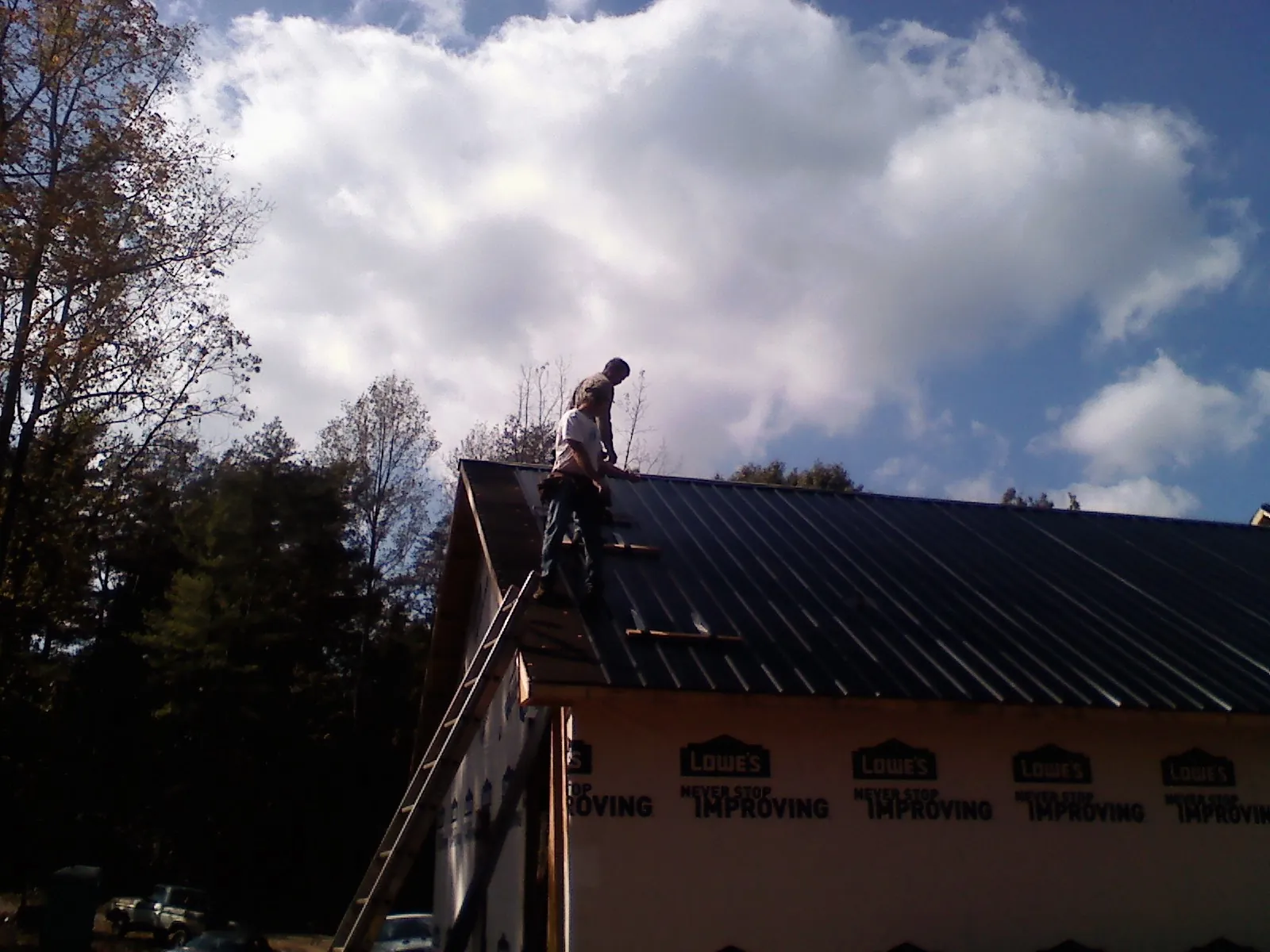 Roofer fastening dark metal panels high against a cloudy sky, from a Roof Inspection job in Marshall